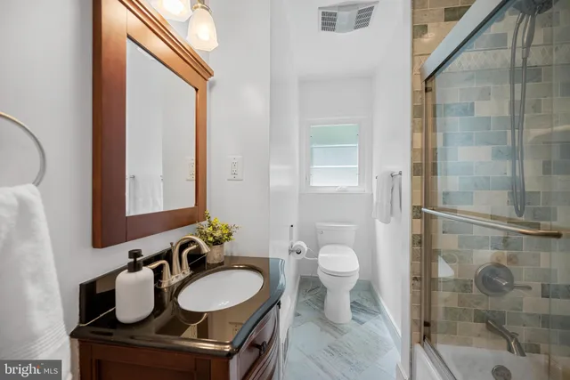 a bathroom with a granite countertop sink a toilet a mirror and shower