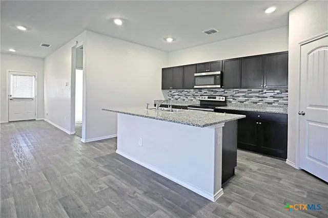 a kitchen with stainless steel appliances granite countertop a stove top oven a refrigerator and a sink