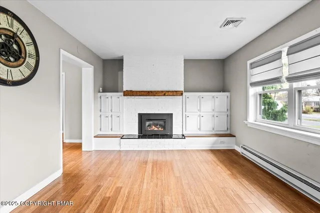a view of a livingroom with furniture a fireplace wooden floor and windows