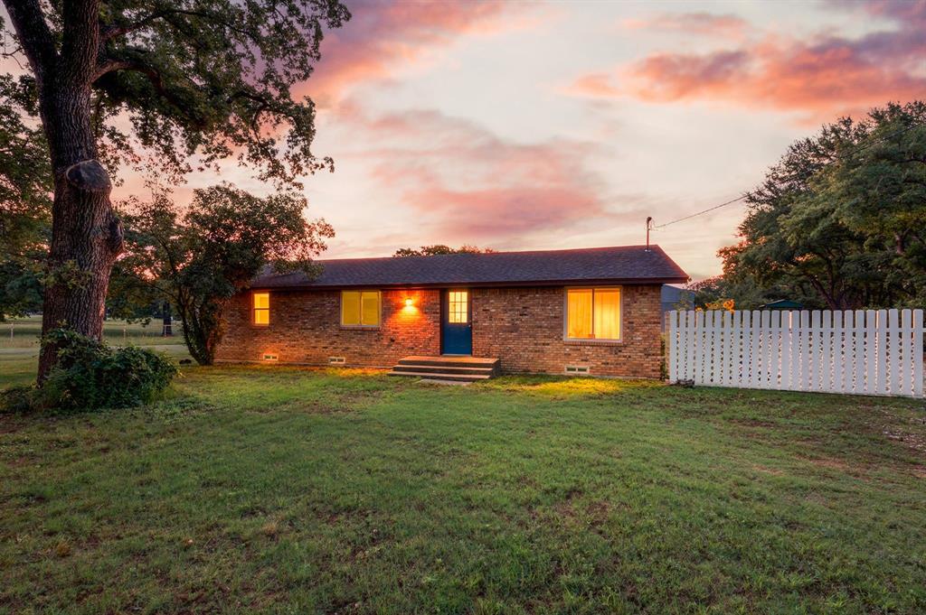 3900 Moseley Road Cross Roads, TX 76227 - Photo 31 of 36 Brick exterior residence featuring a prominent blue entry door, an elevated entryway with steps, and a white picket fence