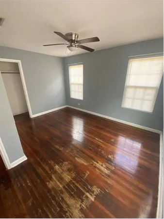 an empty room with wooden floor fan and windows