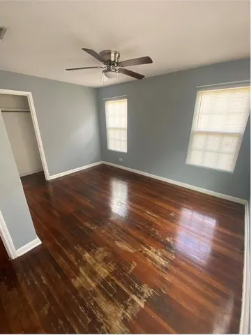 an empty room with wooden floor fan and windows