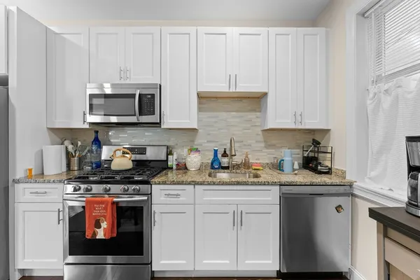 a kitchen with stainless steel appliances a stove a sink a refrigerator white cabinets and wooden floor