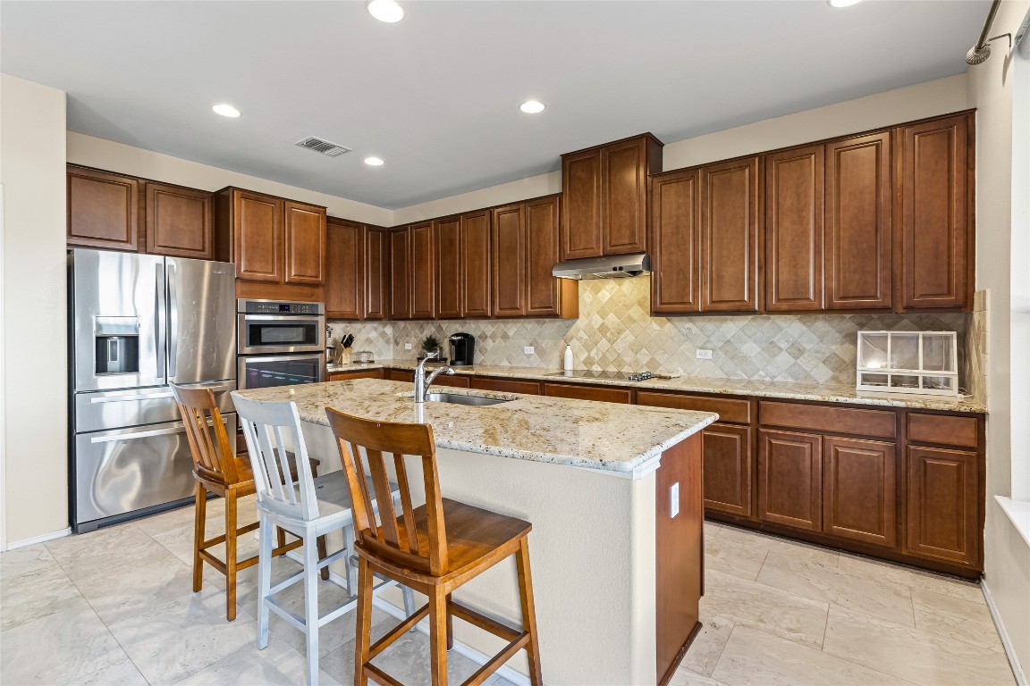 920 Autumn Sage Way Pflugerville, TX 78660 - Photo 19 of 30 a kitchen with kitchen island granite countertop wooden cabinets a refrigerator oven a sink and dishwasher