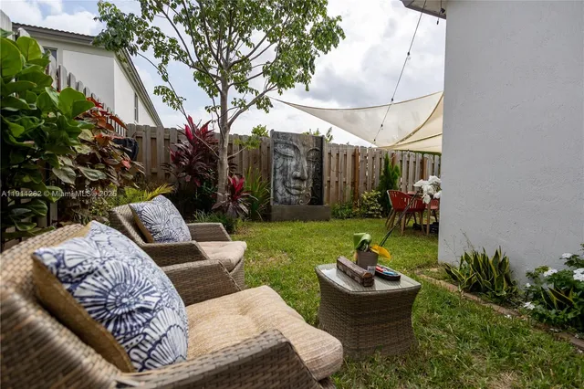 a view of a backyard with couches table and chairs potted plants and large tree