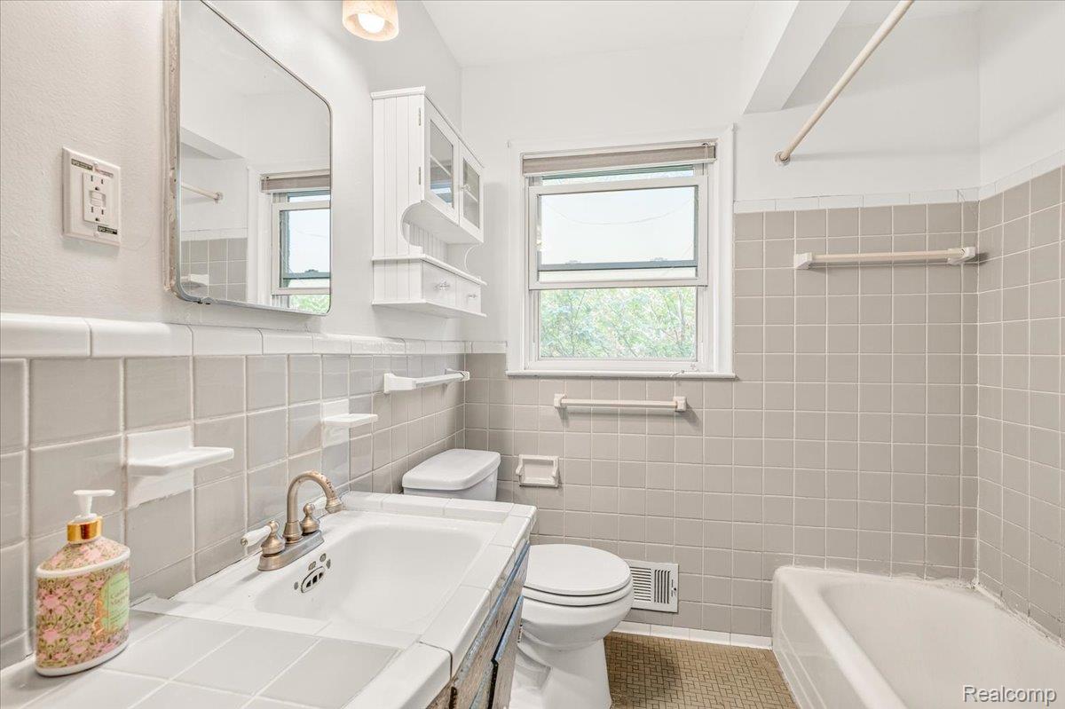 11802 Columbia Street Redford, MI 48239 - Photo 12 of 39 Bathroom featuring a tiled sink vanity, wall-mounted mirror, and a built-in bathtub with tiled surround.