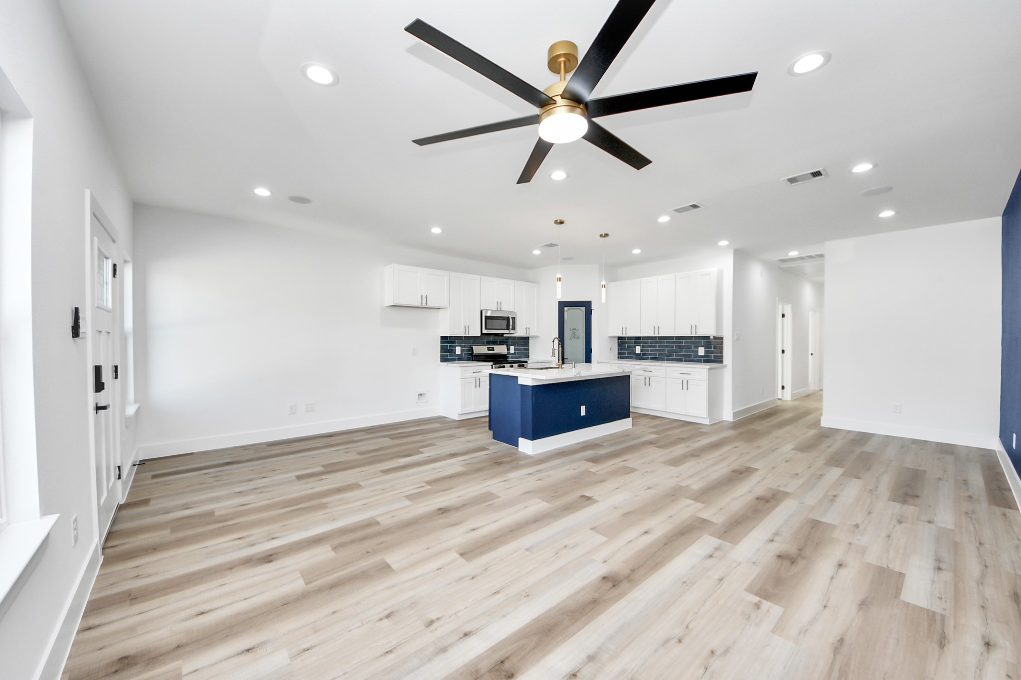4606 Mallow Street Houston, TX 77051 - Photo 12 of 31 Modern open-plan kitchen and living area. It features light flooring, white cabinetry, a central island with navy accents, and stainless steel appliances. Recessed lighting and a sleek ceiling fan add a contemporary touch. The space is bright and welcoming.