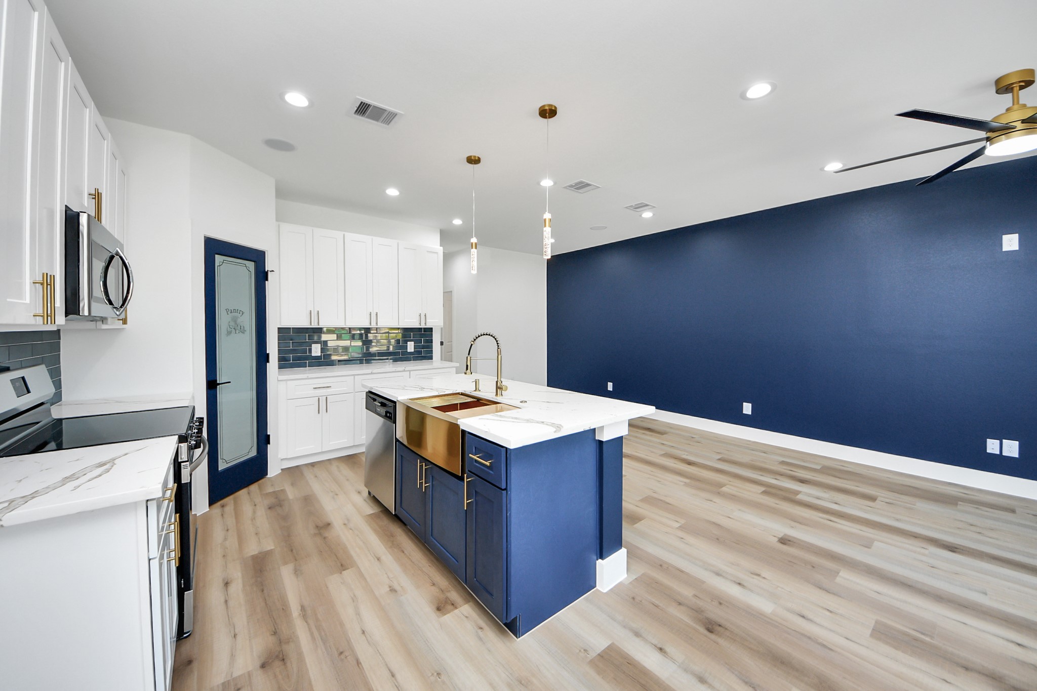 4606 Mallow Street Houston, TX 77051 - Photo 17 of 31 Modern, open-concept kitchen and living area. It features a stylish blue and white color scheme, a large kitchen island with a farmhouse sink, and contemporary lighting fixtures. The space has sleek stainless steel appliances, ample cabinetry, and a striking blue accent wall, complemented by light wood flooring.