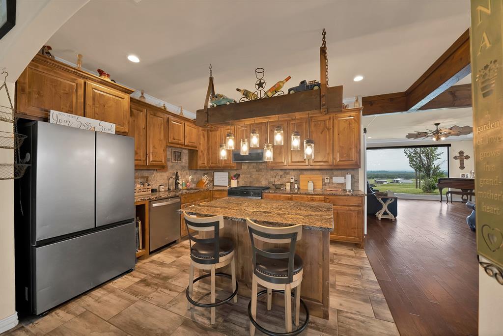 100 Shadle Ridge Court Poolville, TX 76487 - Photo 11 of 40 Kitchen featuring wood cabinetry, granite countertops, tile backsplash, and a central island with bar seating