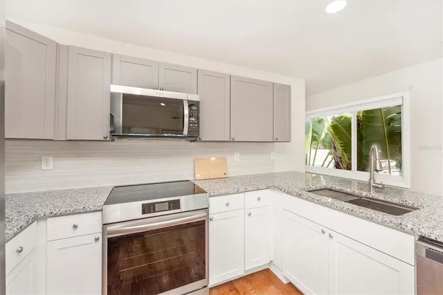 a kitchen with granite countertop a stove a sink and white cabinets with wooden floor next to windows