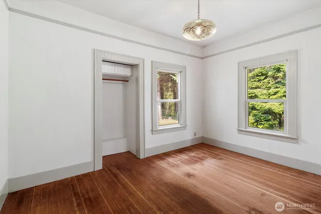 an empty room with wooden floor chandelier fan and windows