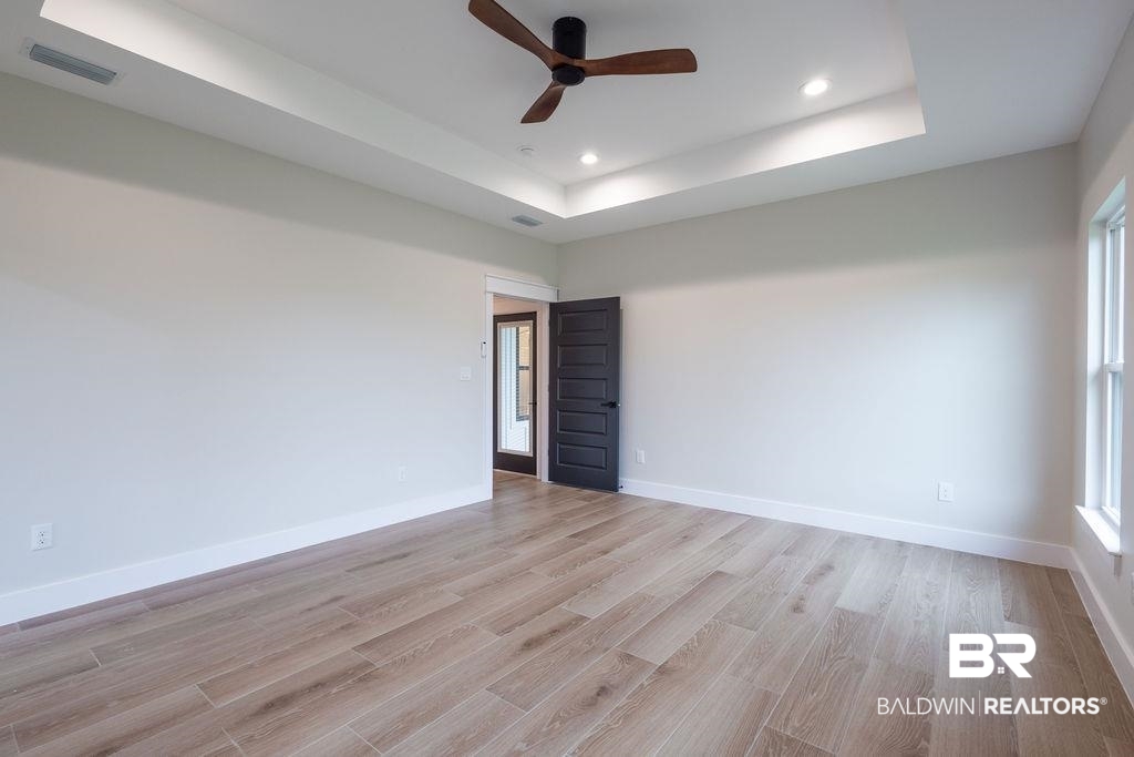 13066 Gopher Court Elberta, AL 36530 - Photo 16 of 38 Spacious room featuring wood-finish flooring, a tray ceiling with recessed lighting and a ceiling fan, and white baseboards.