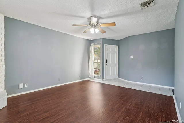 a view of an empty room with wooden floor and a ceiling fan