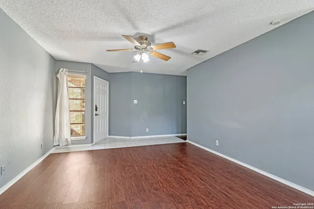 an empty room with wooden floor chandelier fan and windows