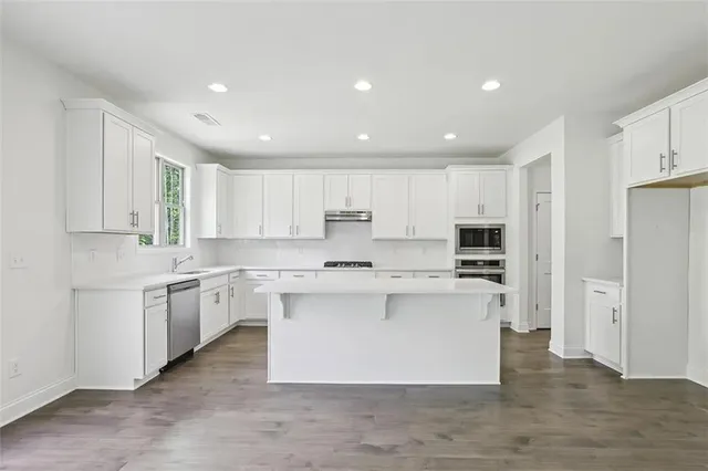 a large kitchen with stainless steel appliances a sink a stove a refrigerator and white cabinets