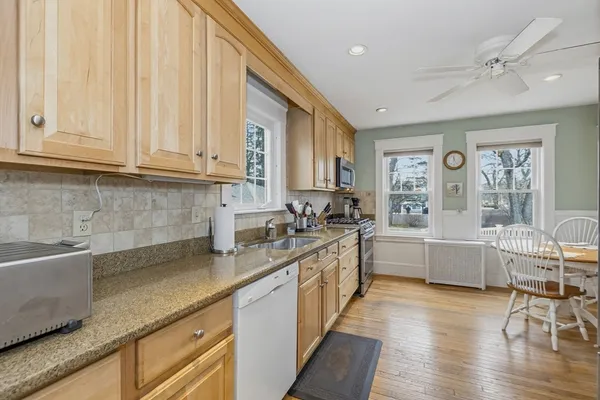 a large white kitchen with granite countertop a sink and dishwasher a stove with wooden floor