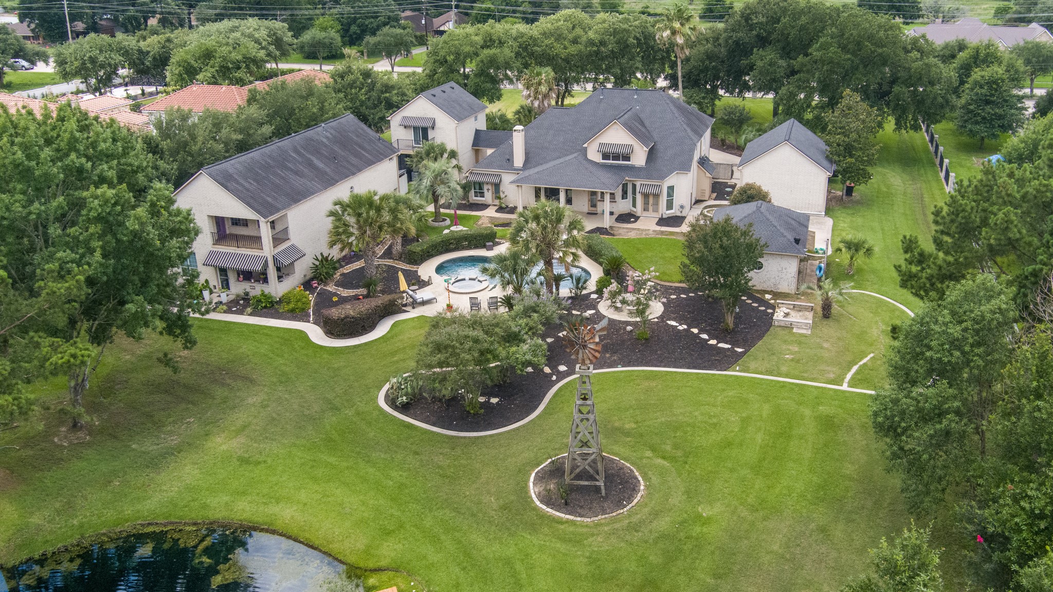13914 Skinner Road Cypress, TX 77429 - Photo 1 of 50 Aerial view of the private estate showcasing multiple residences, a pool and spa, mature trees, manicured grounds, a decorative windmill, and peaceful pond views.