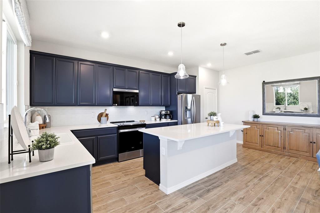 740 Rioja Drive Minneola, FL 34715 - Photo 13 of 33 a large kitchen with stainless steel appliances kitchen island granite countertop a stove a sink dishwasher and a refrigerator with wooden floor