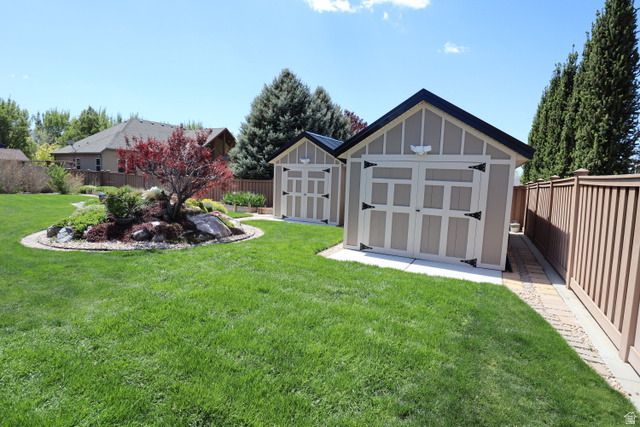 1055 North 1000 East Mapleton, UT 84664 - Photo 102 of 112 Expansive green lawn featuring two gable-roof storage sheds, a decorative rock garden with a red-leaf tree, a tan privacy fence, and a paver stone walkway