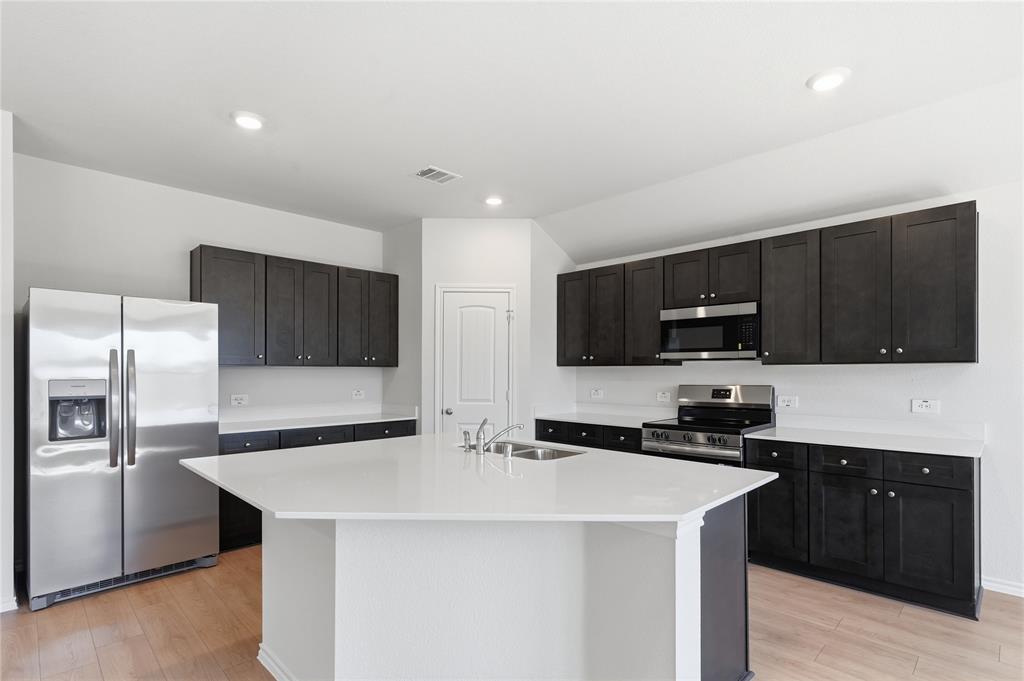 1905 Reveille Way Terrell, TX 75160 - Photo 4 of 6 Kitchen featuring a central island with an undermount double-basin sink, stainless steel appliances, dark wood-finish cabinetry, light countertops, and wood-finish flooring