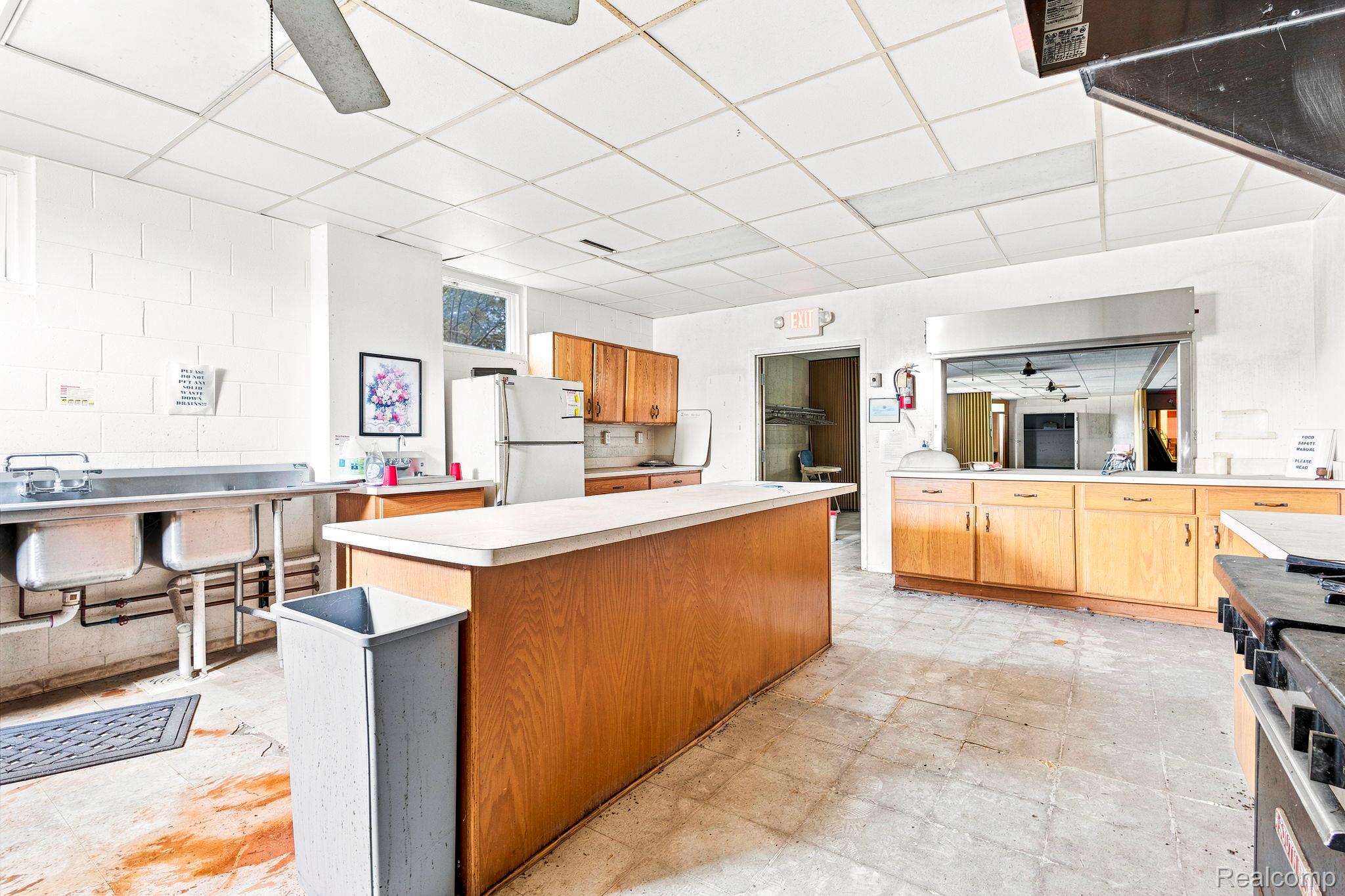 9735 Dolan Road Columbus, MI 48063 - Photo 58 of 63 Spacious kitchen area featuring tile flooring, a large central island with a solid surface countertop, wood-finish cabinetry, a stainless steel commercial-style sink, and a service window with a stainless steel hood