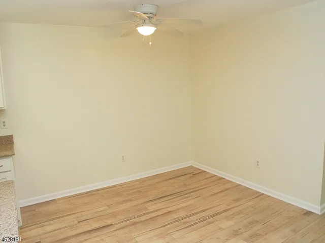 a view of an empty room with wooden floor and a ceiling fan