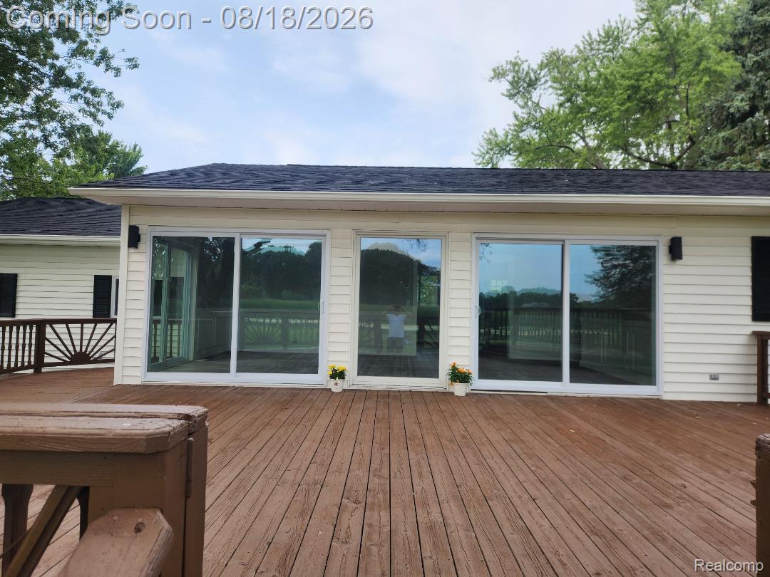 32563 Sutton Road New Baltimore, MI 48047 - Photo 11 of 43 Expansive wood deck with a built-in railing, three large sliding glass doors, light-colored siding, and a dark shingle roof