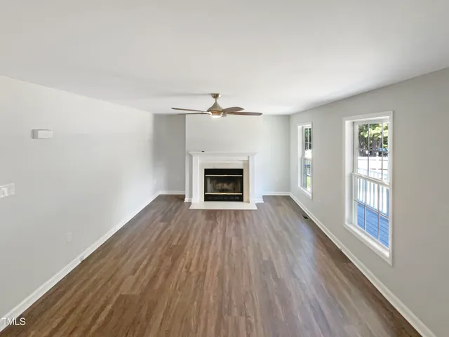 an empty room with wooden floor fireplace and windows
