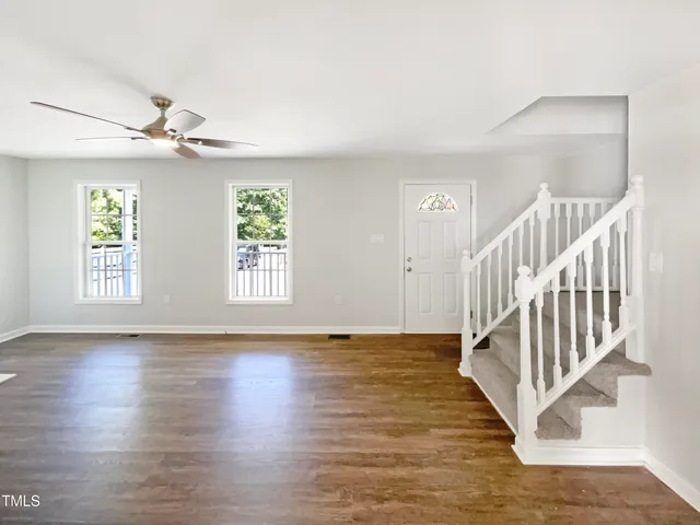 a view of an empty room with wooden floor and a ceiling fan