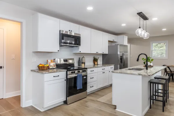 a kitchen with stainless steel appliances granite countertop a stove top oven a sink a refrigerator and white cabinets