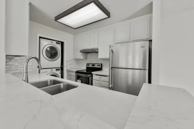 a kitchen with granite countertop a refrigerator a sink and white cabinets