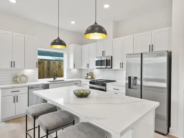 a kitchen with stainless steel appliances granite countertop a sink a stove a refrigerator and white cabinets with wooden floor