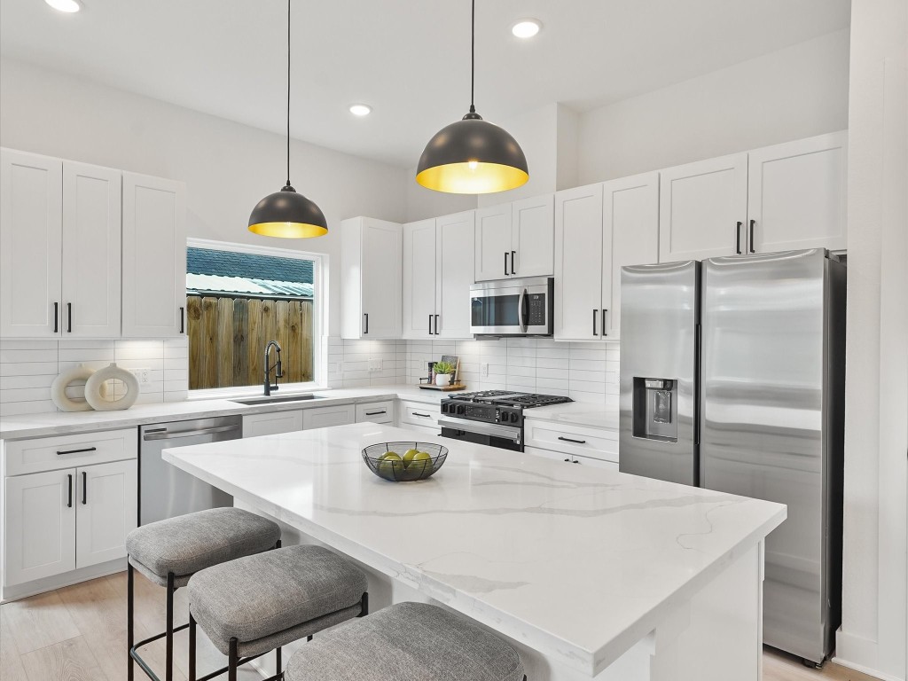a kitchen with stainless steel appliances granite countertop a sink a stove a refrigerator and white cabinets with wooden floor