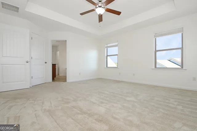 an empty room with chandelier fan and windows