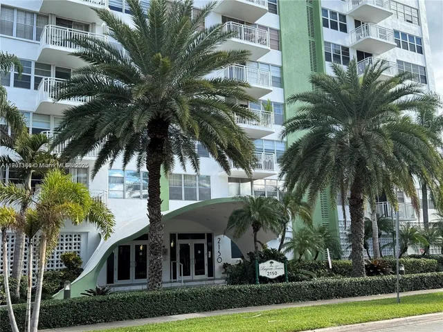 a front view of multi story residential apartment building with yard and parking