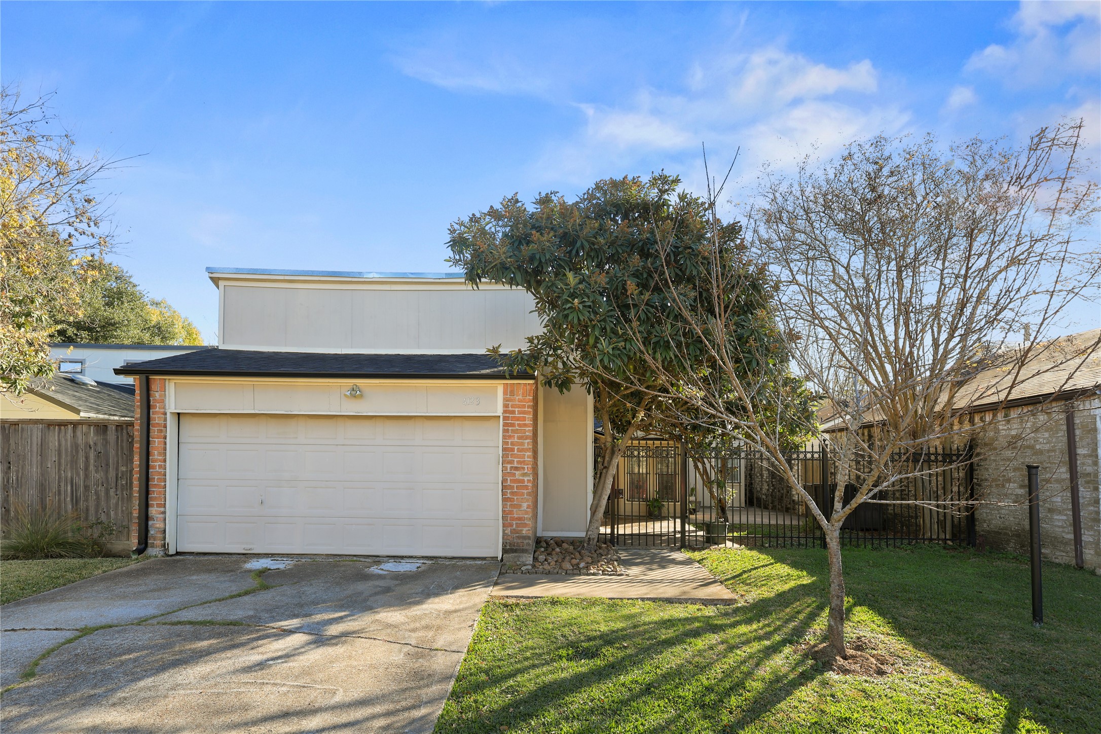 4123 Yupon Ridge Drive Houston, TX 77072 - Photo 1 of 22 This photo shows a modern, two-story home with a clean, minimalist facade featuring a two-car garage. The front yard has a small lawn with a couple of trees, and the property is enclosed with a wooden fence on one side. The setting is bright and welcoming under a clear blue sky.