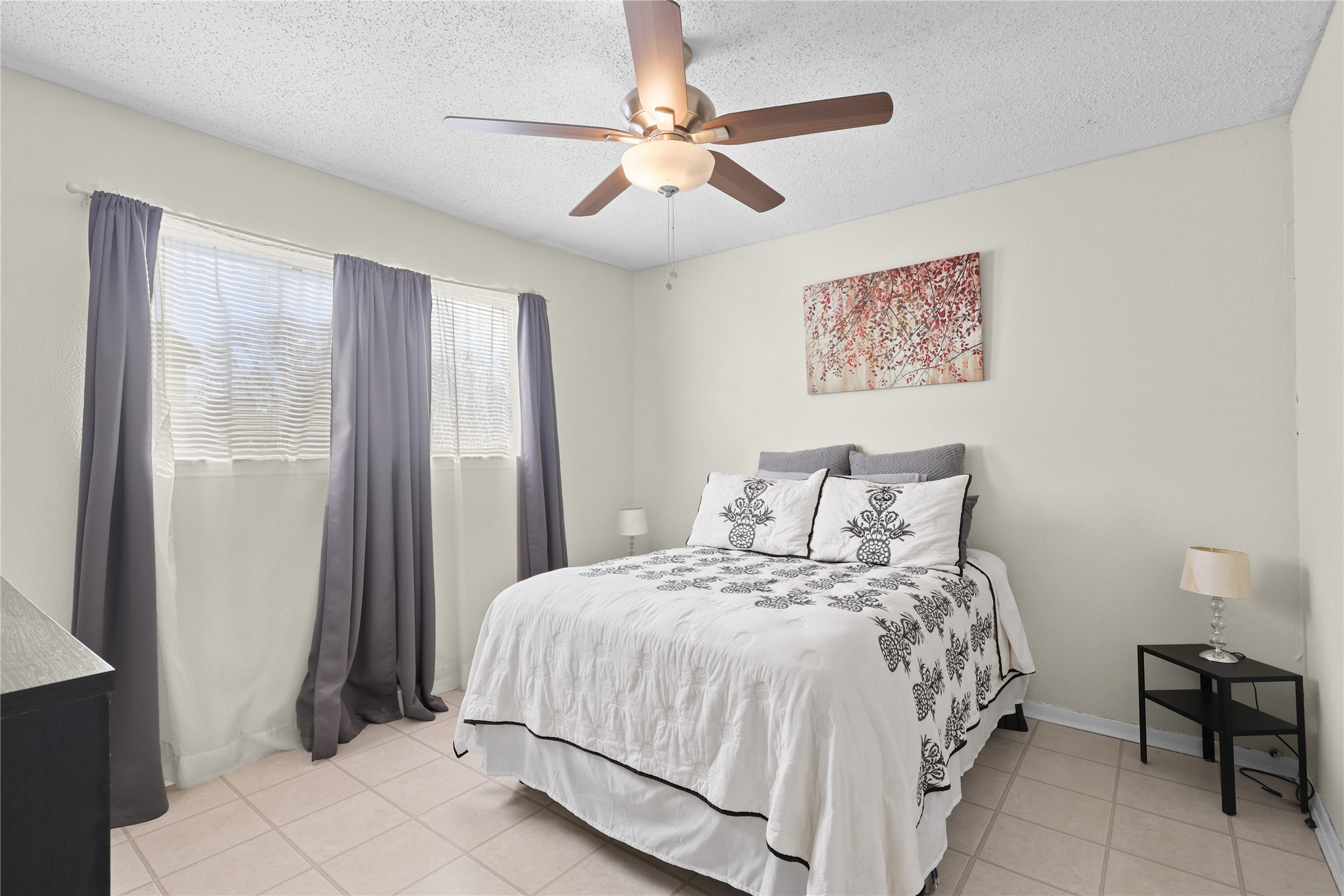 4123 Yupon Ridge Drive Houston, TX 77072 - Photo 11 of 22 This cozy bedroom features a comfortable bed with elegant bedding, a ceiling fan, and ample natural light from a window with sheer and dark curtains. The room is accented with a simple piece of wall art and a small side table with a lamp.
