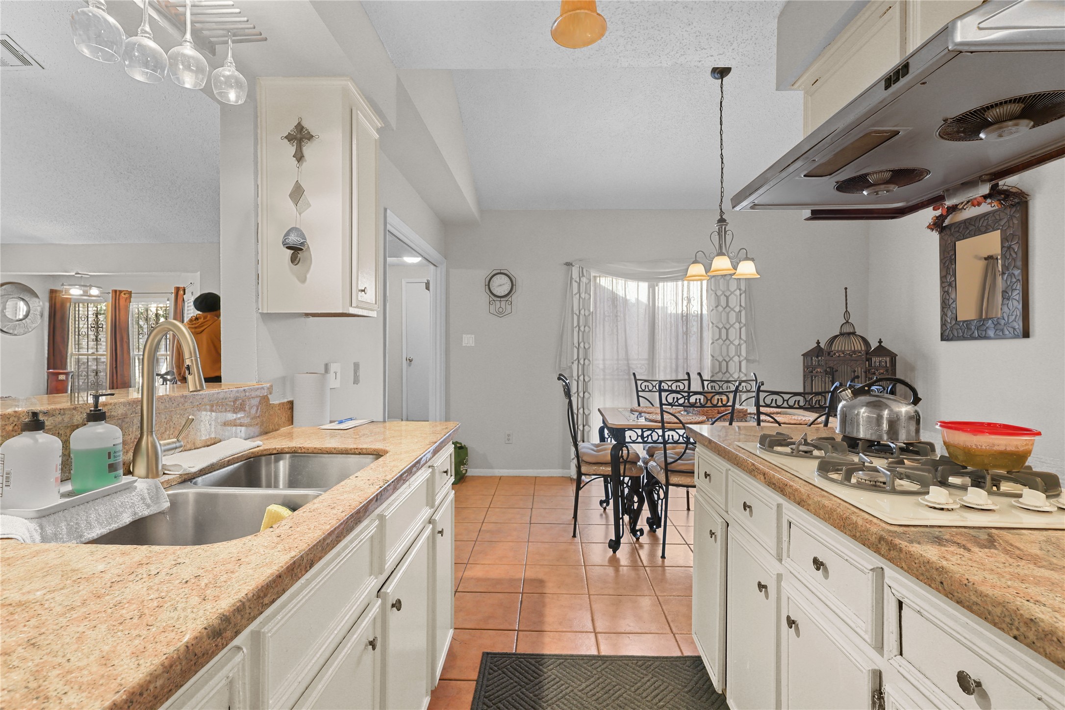 4123 Yupon Ridge Drive Houston, TX 77072 - Photo 14 of 22 This photo showcases a bright kitchen with granite countertops, a double sink, and a gas stove. It opens to a cozy dining area with tiled floors and a stylish light fixture above the table.