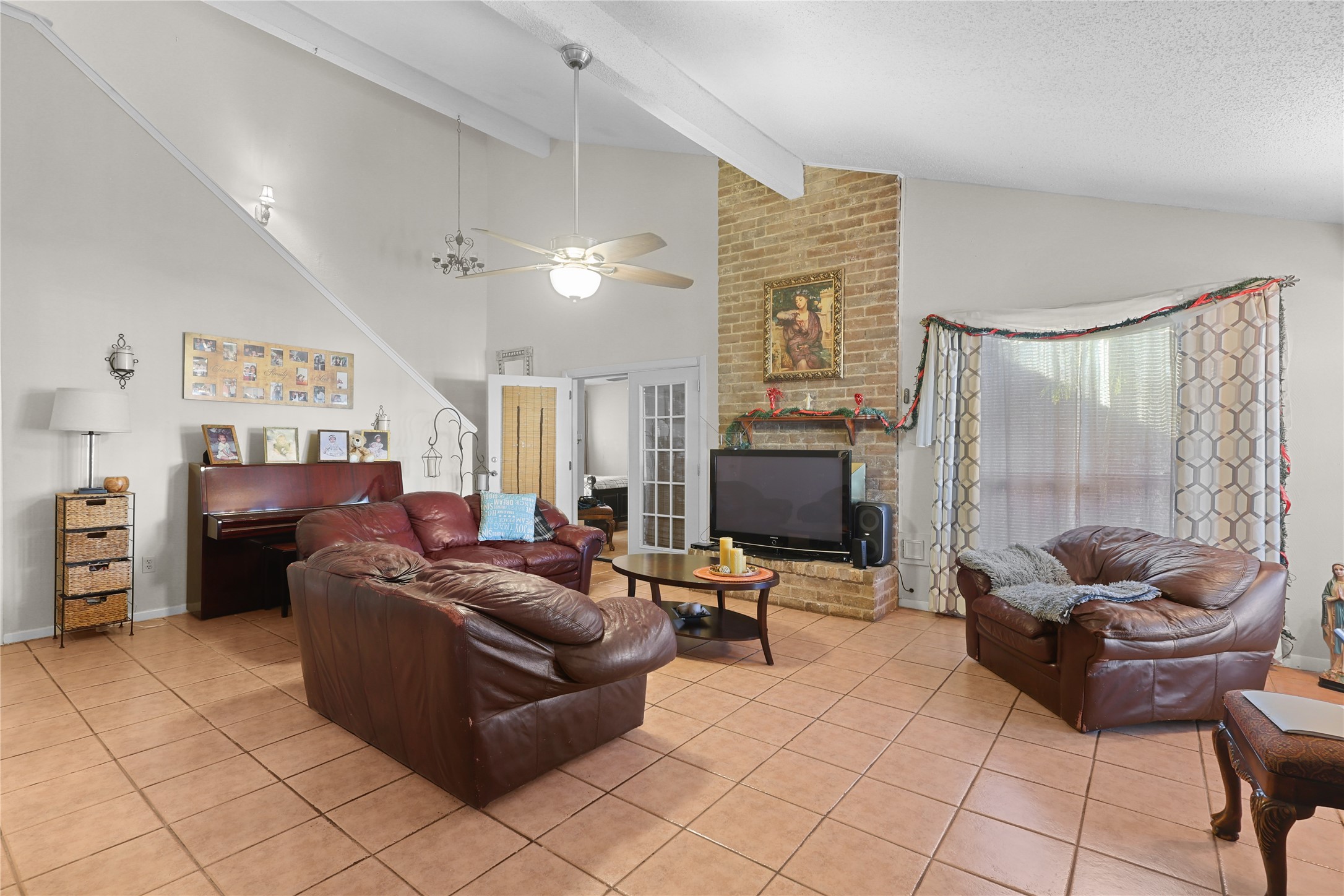4123 Yupon Ridge Drive Houston, TX 77072 - Photo 21 of 22 This spacious living room features high ceilings with exposed beams, a cozy brick fireplace, and large windows for natural light. It includes comfortable leather seating, a piano, and tile flooring, creating a warm and inviting atmosphere for relaxation and entertainment.