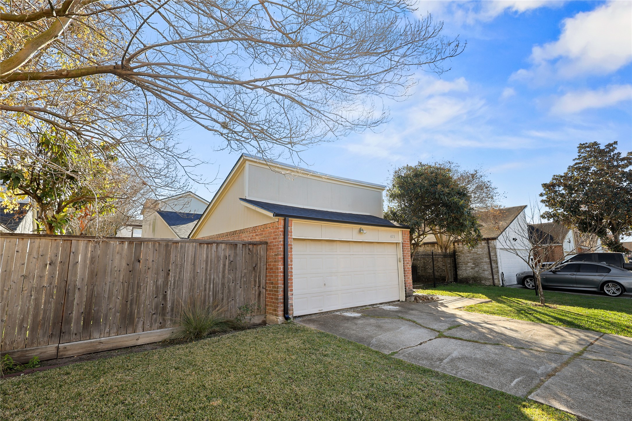 4123 Yupon Ridge Drive Houston, TX 77072 - Photo 3 of 22 This photo features a suburban home with a two-car garage and a well-maintained driveway. The yard is grassy and bordered by a wooden fence, with trees providing shade and adding to the property's charm. The neighborhood appears quiet and residential.