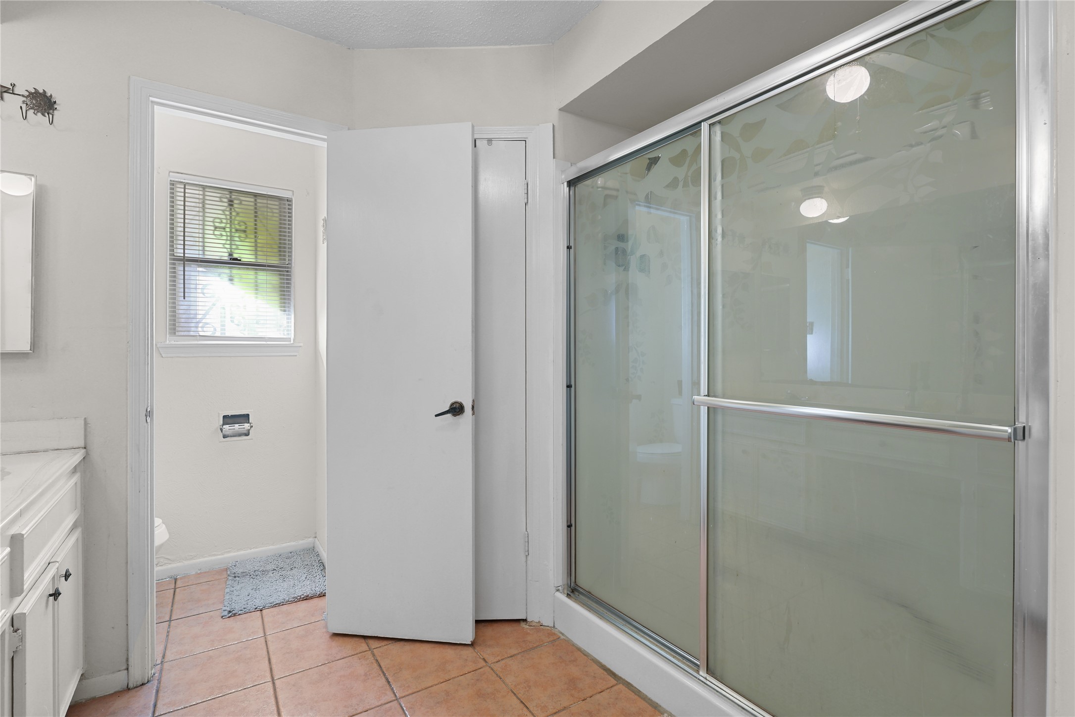 4123 Yupon Ridge Drive Houston, TX 77072 - Photo 7 of 22 Bright bathroom featuring a frosted glass shower, terracotta floor tiles, and a vanity with ample storage. There's a separate toilet area with a window for natural light.