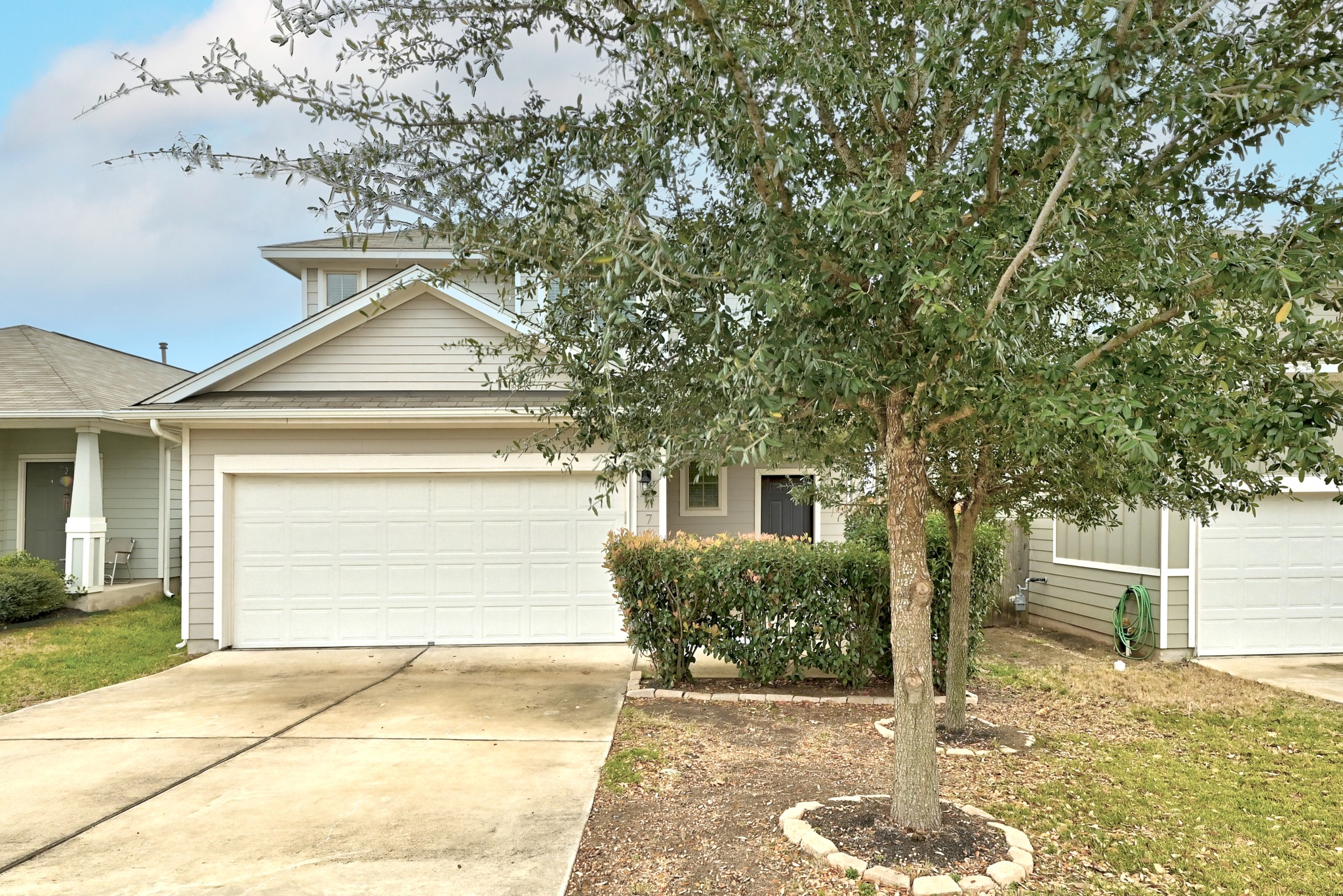 171 Vestral Road Buda, TX 78610 - Photo 2 of 26 View of front of home featuring a two car garage, driveway for extra parking, a composition shingle roof, and a covered front porch with shade trees and landscaping