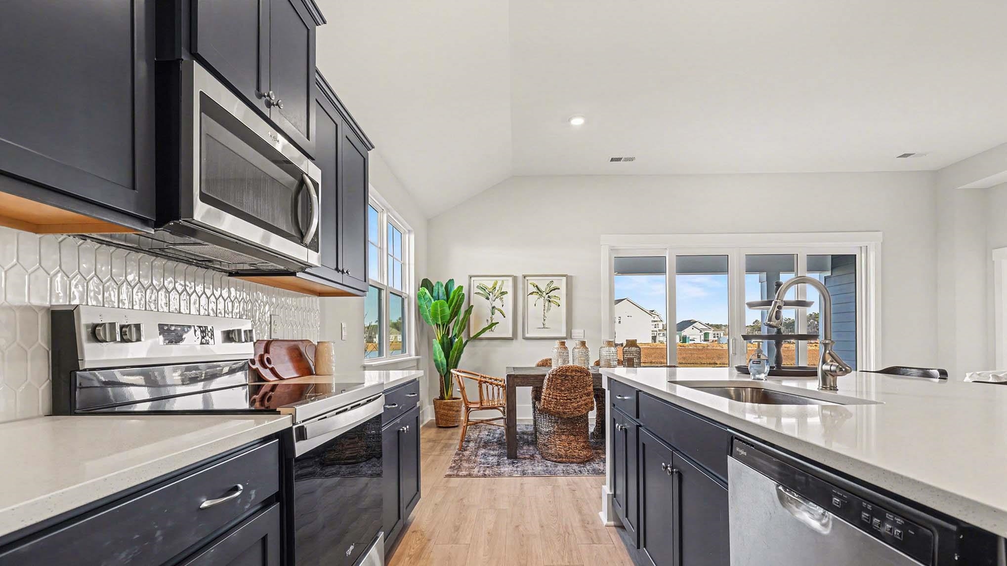 3250 Moss Bridge Lane Myrtle Beach, SC 29579 - Photo 11 of 29 Kitchen with dark cabinetry, appliances with stainless steel finishes, light stone countertops, vaulted ceiling, and light wood finished floors
