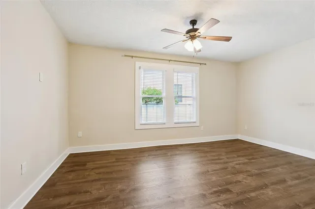 an empty room with wooden floor fan and windows