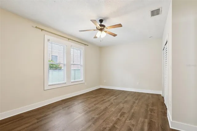 an empty room with wooden floor chandelier fan and windows