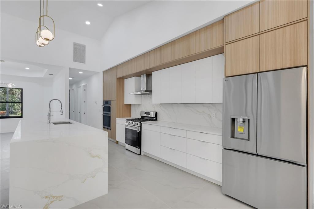 730 29th Street Southwest Naples, FL 34117 - Photo 17 of 50 Kitchen featuring two tone cabinetry, stainless steel appliances, pendant lighting, modern cabinets, and light stone countertops