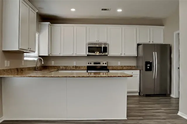 a kitchen with stainless steel appliances granite countertop a stove a refrigerator a sink and white cabinets