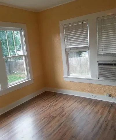 a view of an empty room with wooden floor and a window