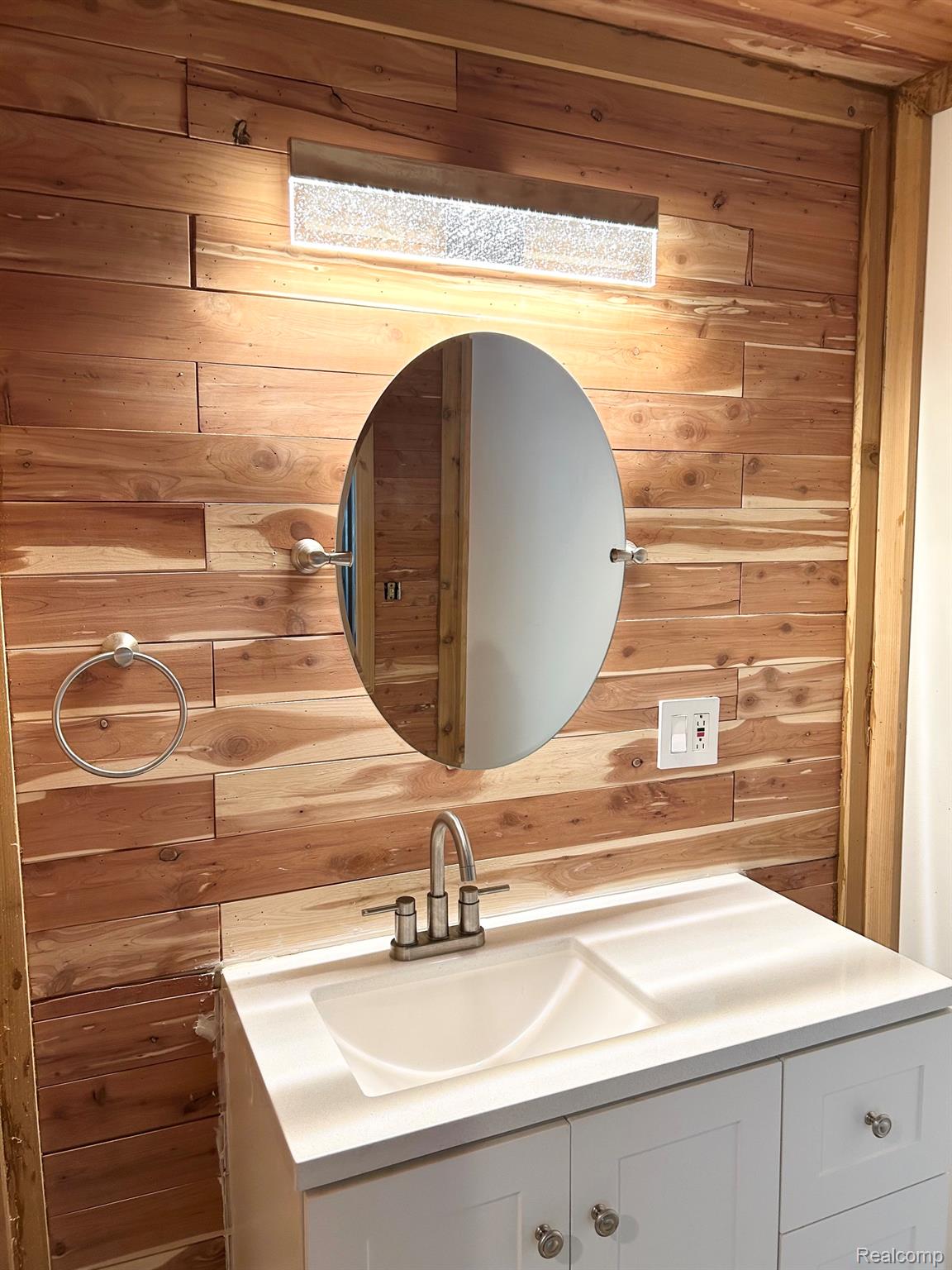 140 Larson Road Attica, MI 48412 - Photo 13 of 41 Wood-paneled accent wall featuring an oval mirror and a contemporary linear light fixture