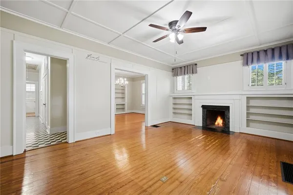 an empty room with wooden floor a fireplace a ceiling fan a fireplace and windows